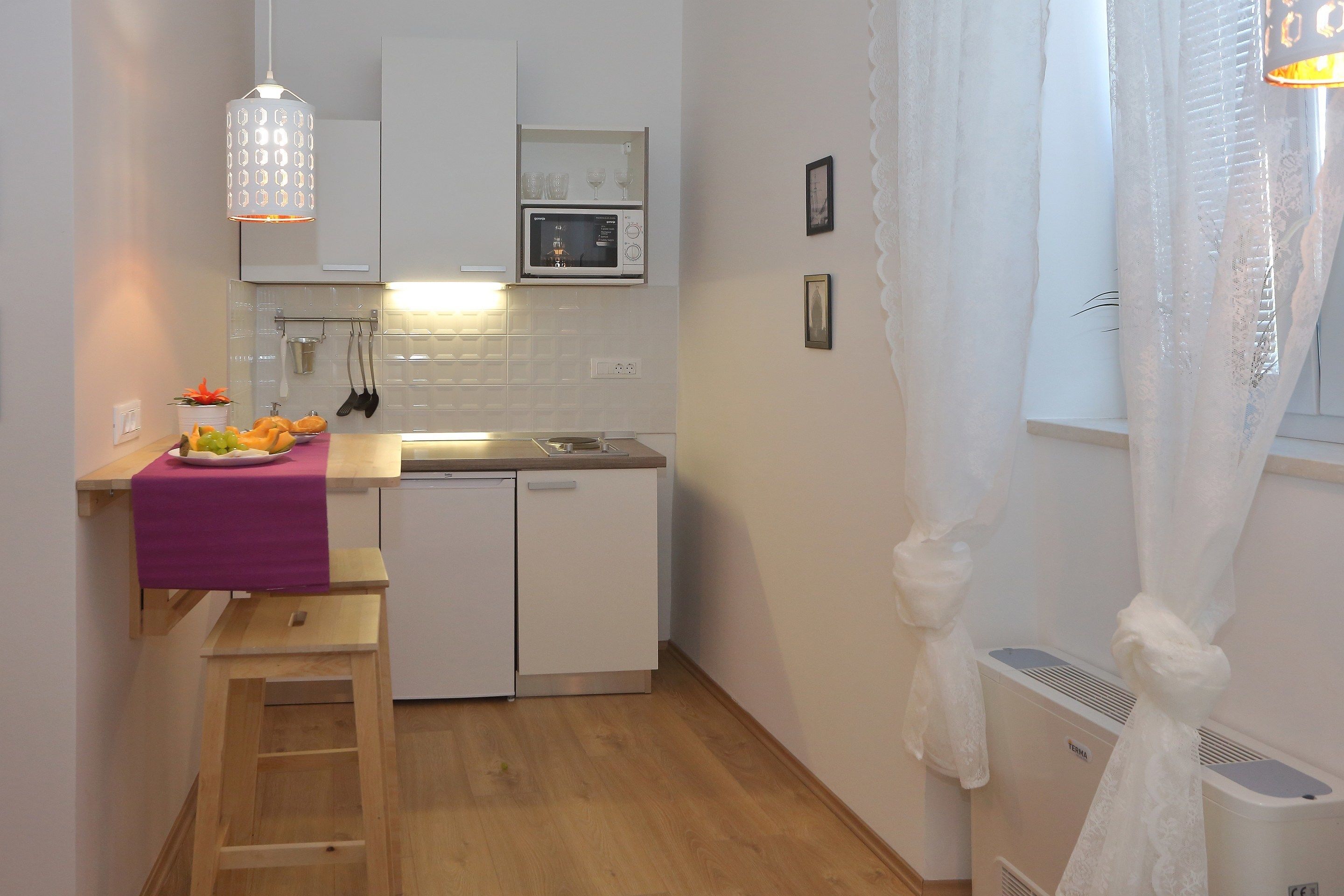Una cocina compacta con microondas, un lavamanos pequeño y un taburete de madera.