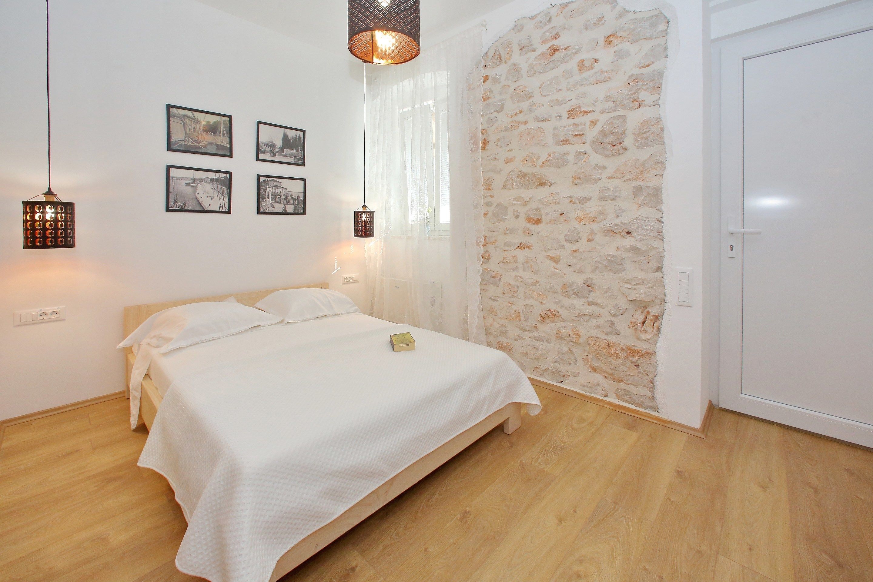 Un dormitorio con cama de madera, ropa de cama blanca, pared de piedra y una puerta blanca.
