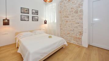 Un dormitorio con cama de madera, ropa de cama blanca, pared de piedra y una puerta blanca.