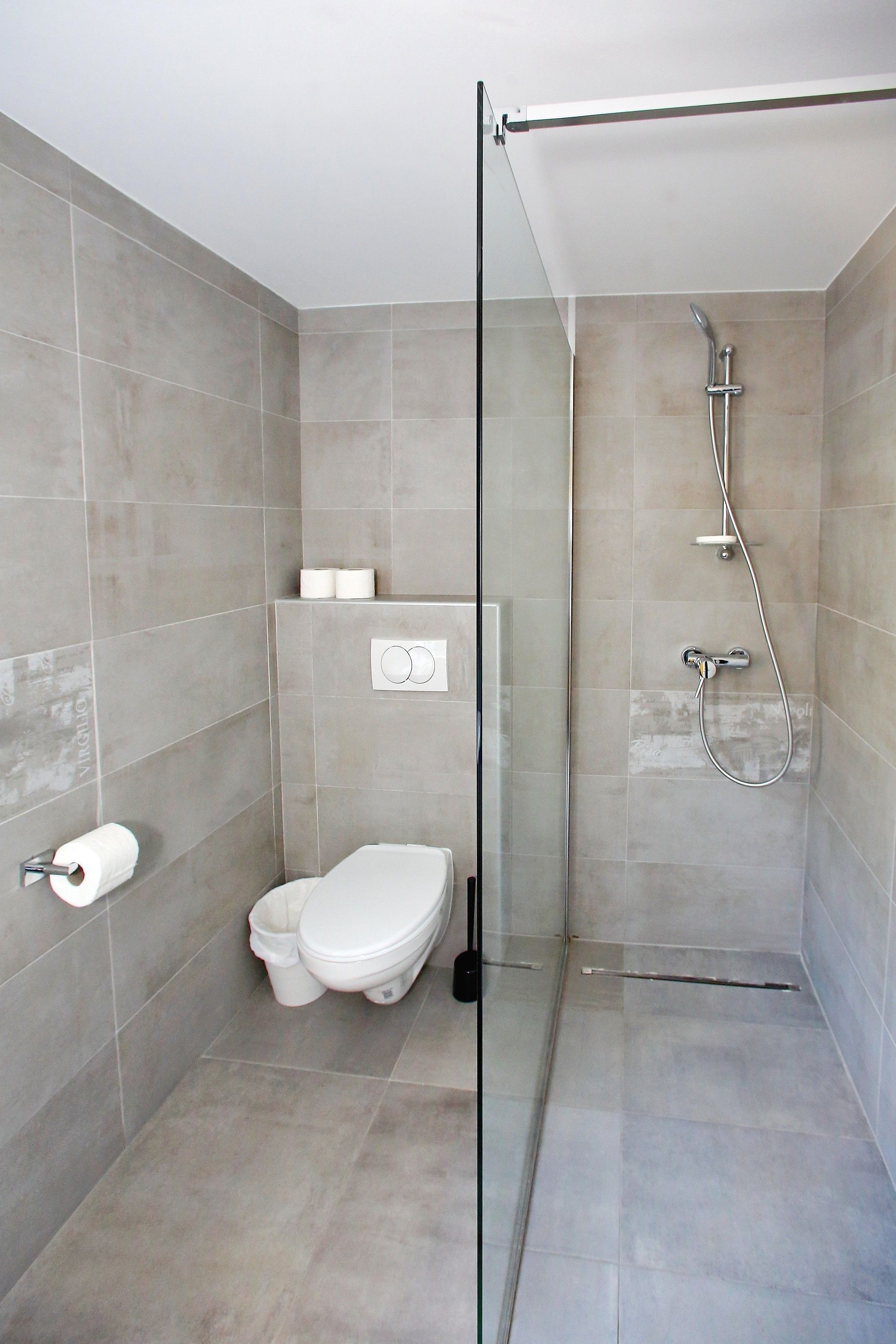Un baño moderno con cabina de ducha de vidrio, inodoro y dispensador de papel higiénico de pared.