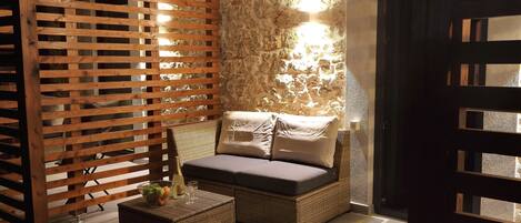 A cozy seating area with a cushioned bench and a small table, a wooden partition, and a stone wall with a light fixture.