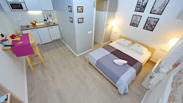A compact hotel room with a bed, bedside table, and a kitchenette.