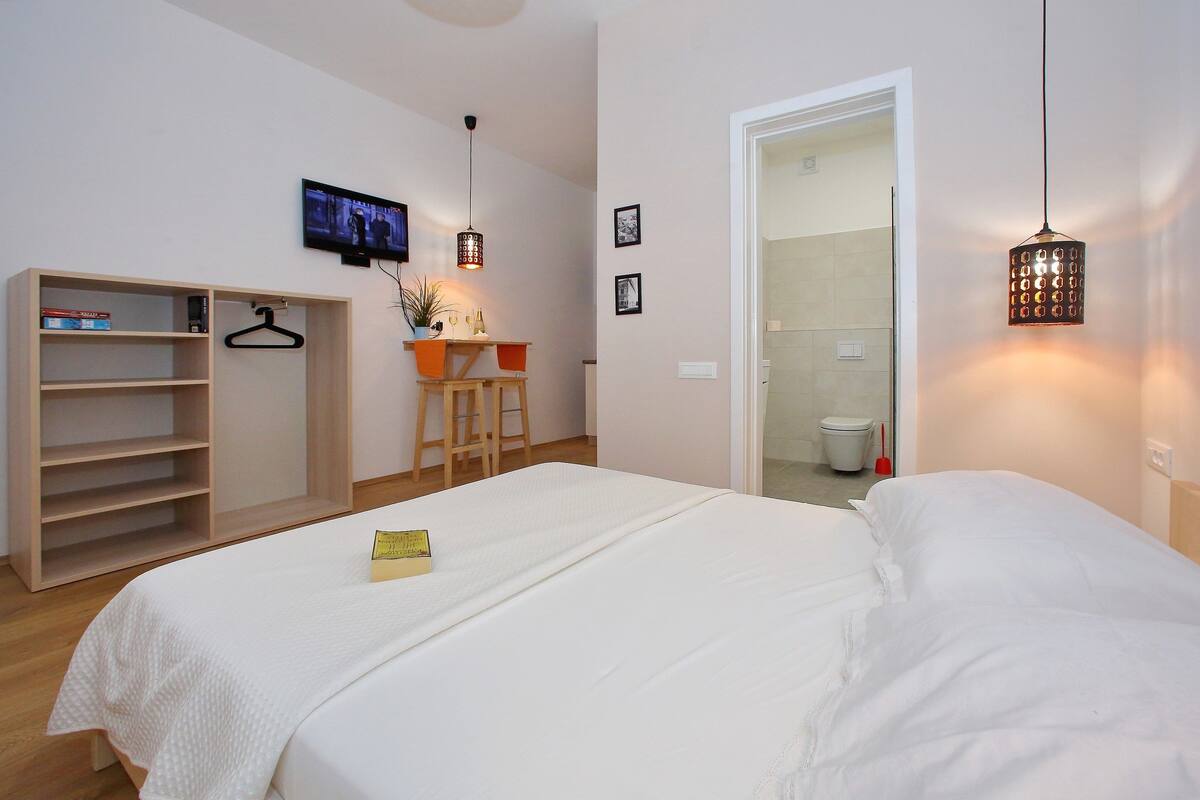 Ein Schlafzimmer mit Bett, Kleiderschrank, Schreibtisch mit Stuhl und Fernseher an der Wand.