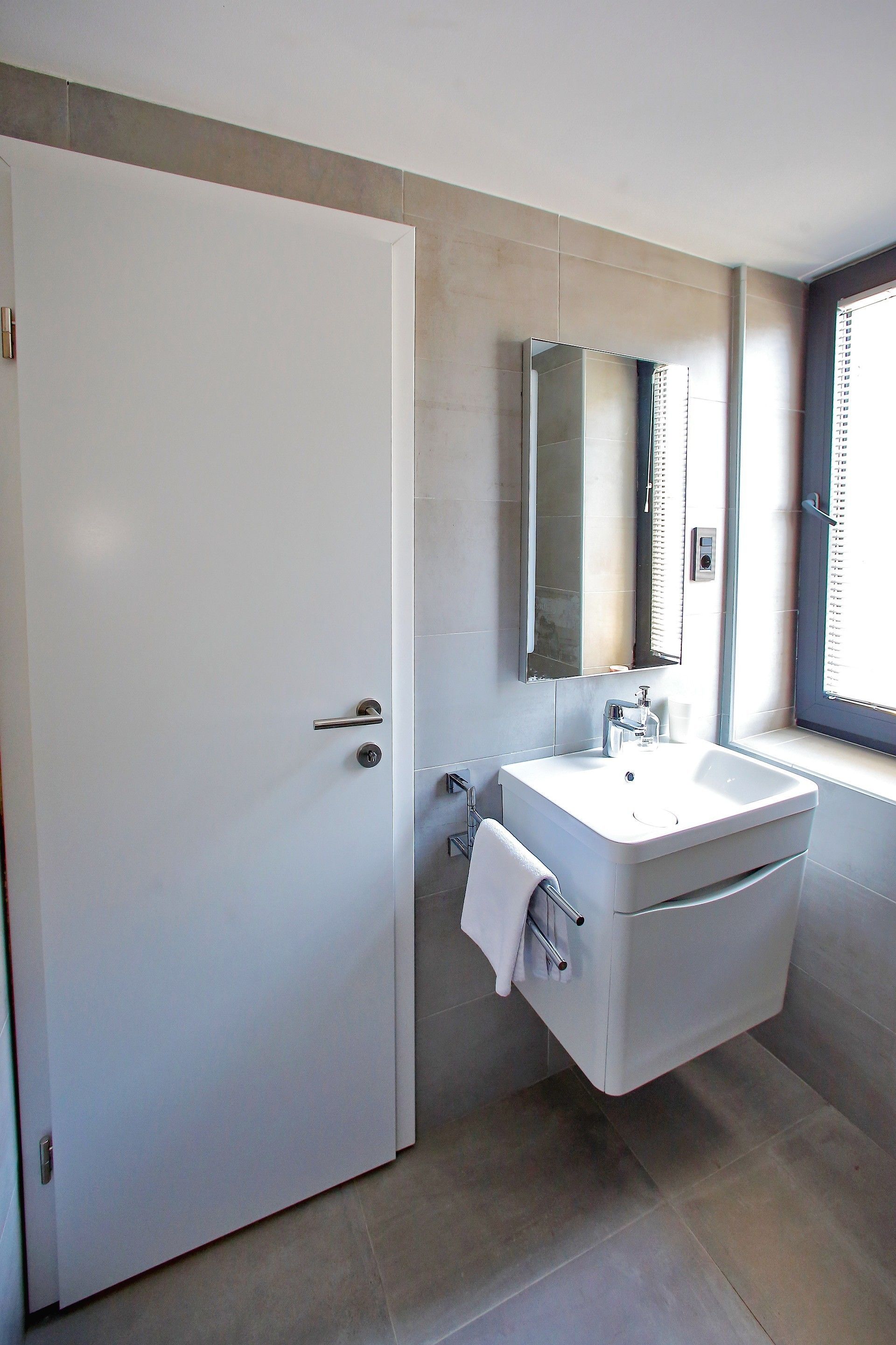 A modern bathroom with a white sink, a large mirror, and a door.