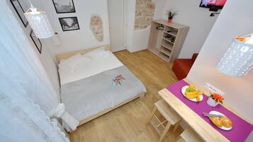 A bedroom with a bed, a desk with breakfast, a TV, and a stone wall.