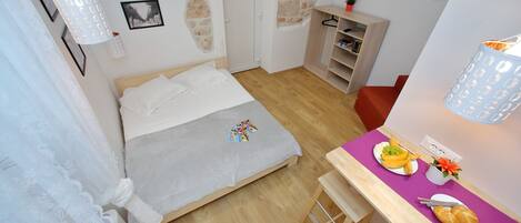 Un dormitorio con cama, escritorio con desayuno, televisión y pared de piedra.