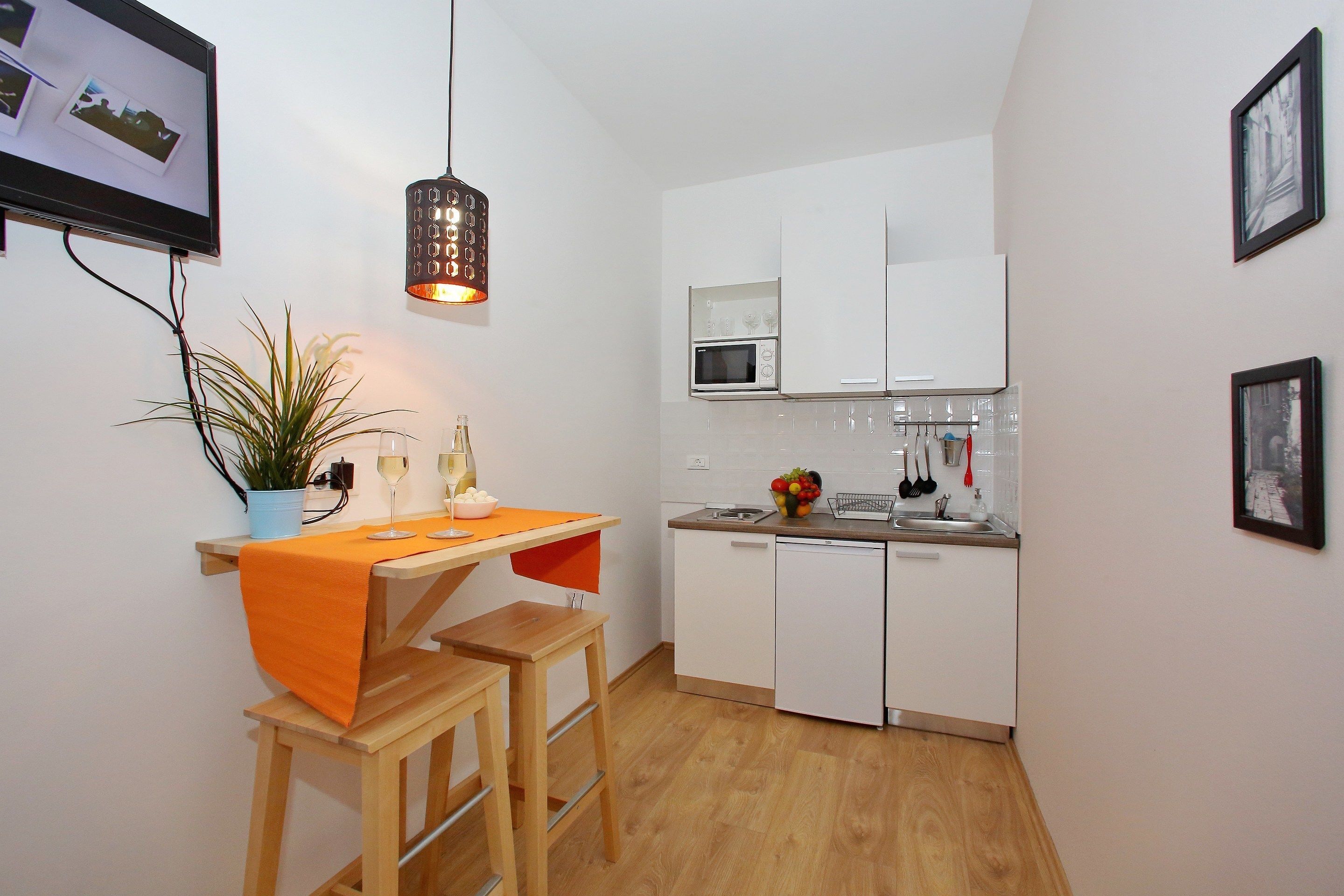 A compact kitchen with a microwave, sink, and white cabinets. There is a small dining area with a wooden table and chairs.