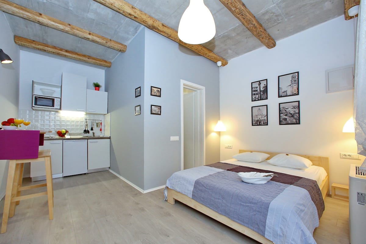 Ein kleines Hotelzimmer mit Bett, Nachttisch und einer Küchenzeile.