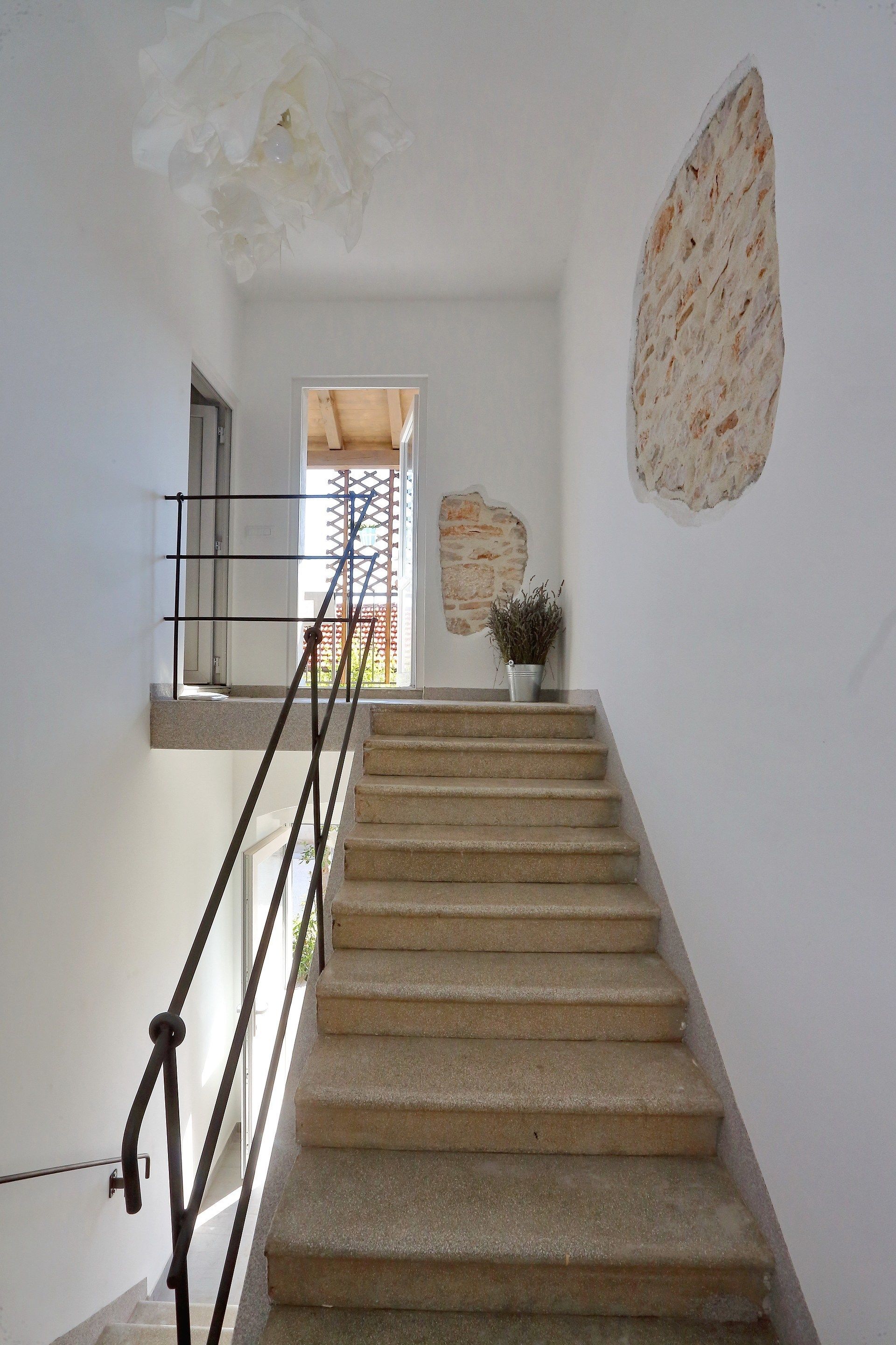 Una escalera con barandilla, una planta en maceta y una pared con un diseño de piedra texturizada.