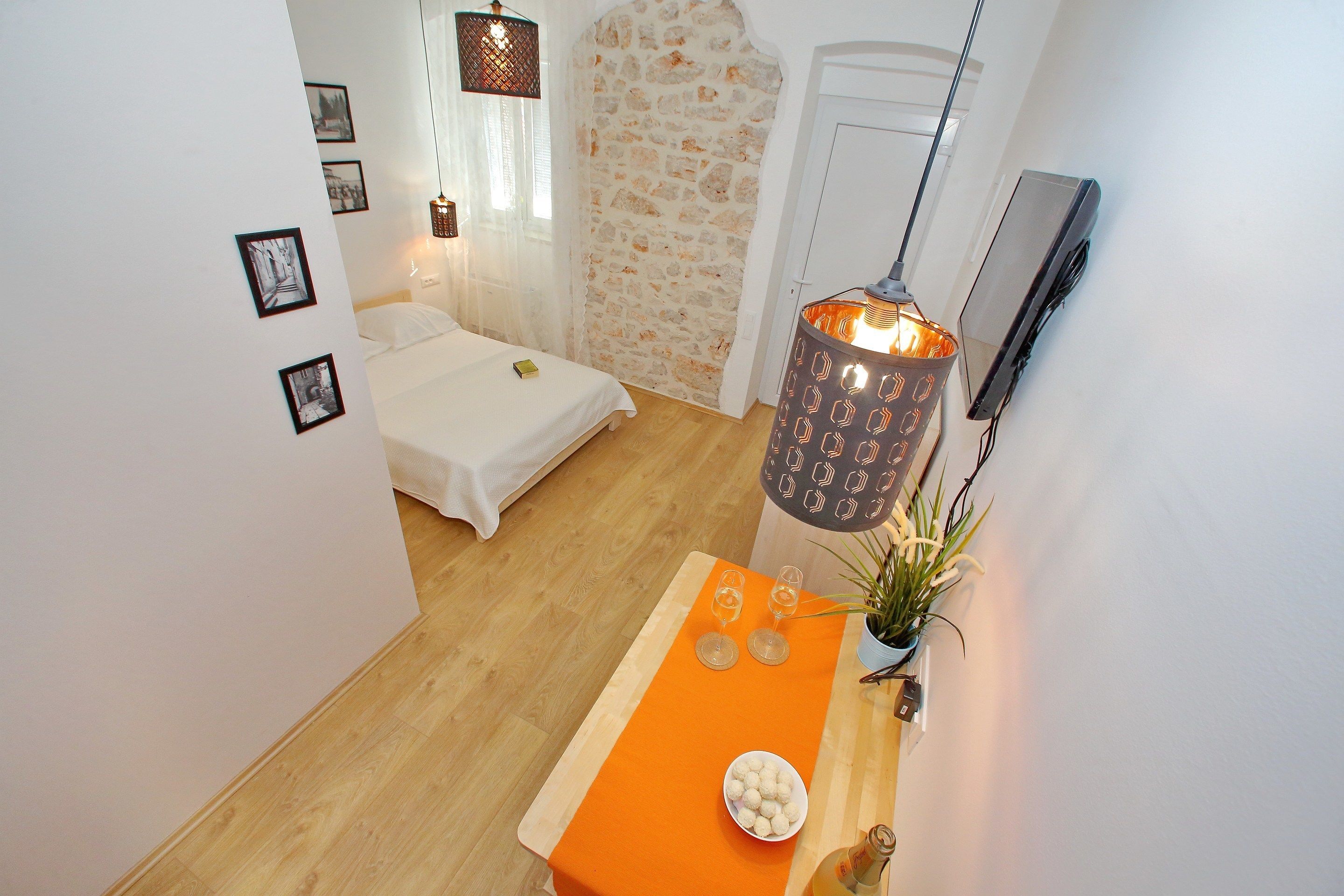 Un dormitorio con una cama, una mesa con fruteros, una planta en maceta y una lámpara colgante.