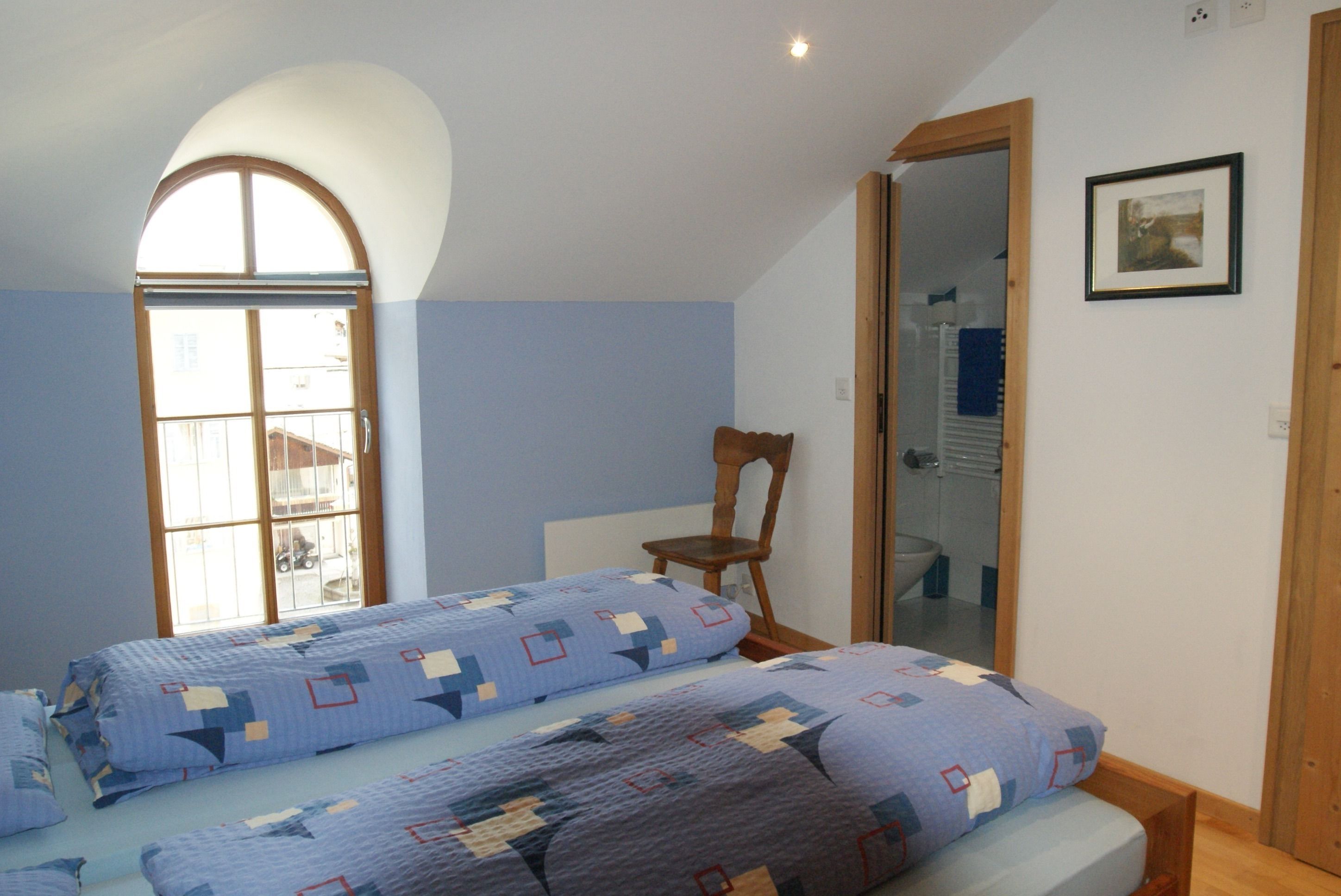 Ein Schlafzimmer mit zwei Betten, einem Fenster, einem Sessel und einer Tür zum Badezimmer.