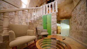 A room with a stone wall, a wooden staircase, a green door, a round glass table, and two armchairs.