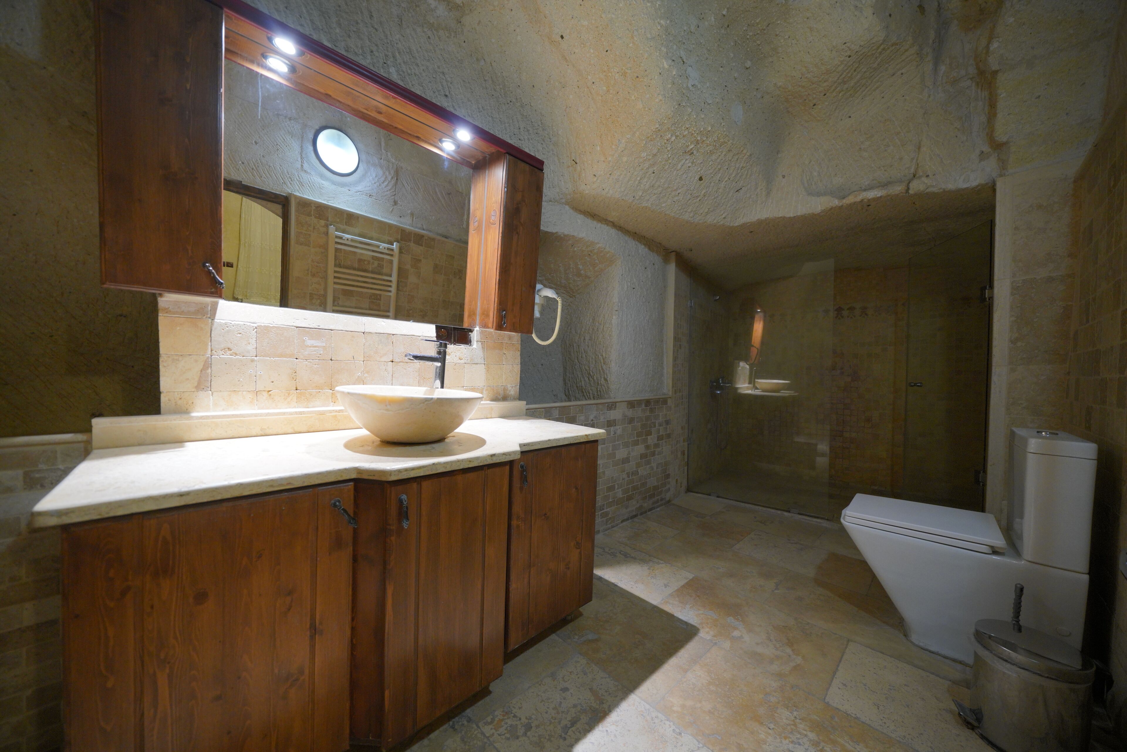 A bathroom with a wooden vanity, a large sink, a mirror, and a shower area.