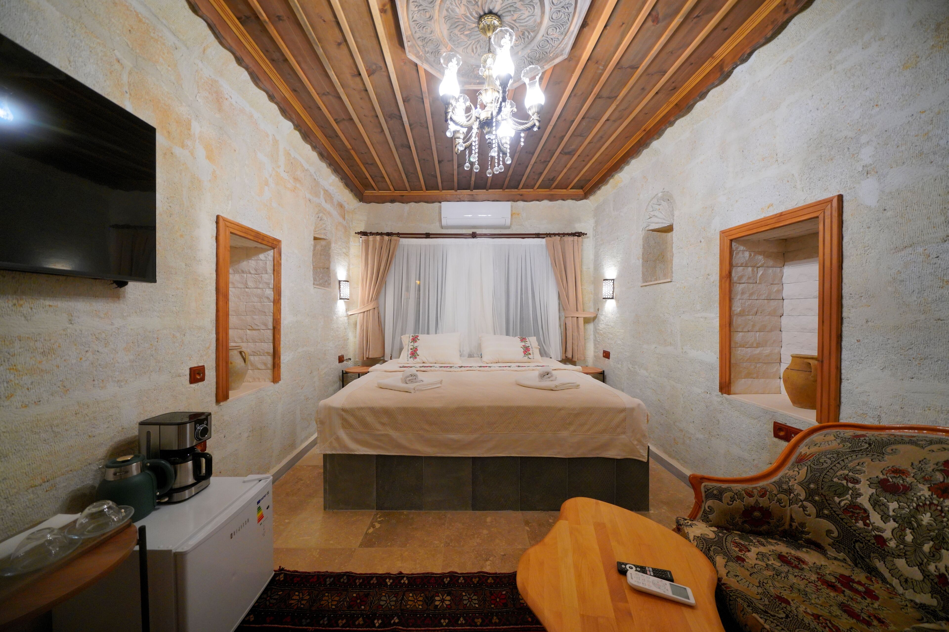 A bedroom with a bed, a TV, a coffee maker, a sofa, and a chandelier.