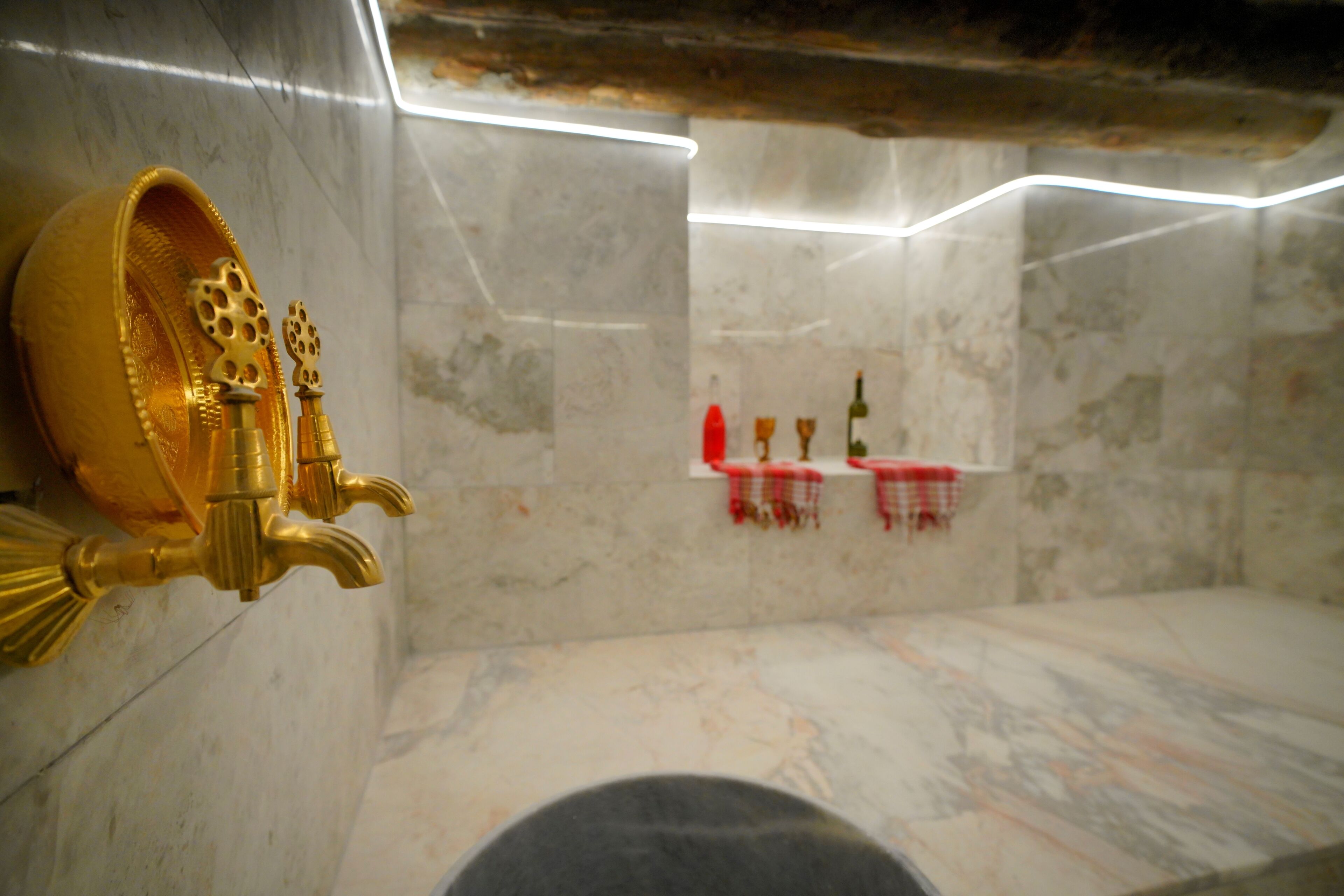 A bathroom with marble walls, a gold faucet, and a red towel rack.
