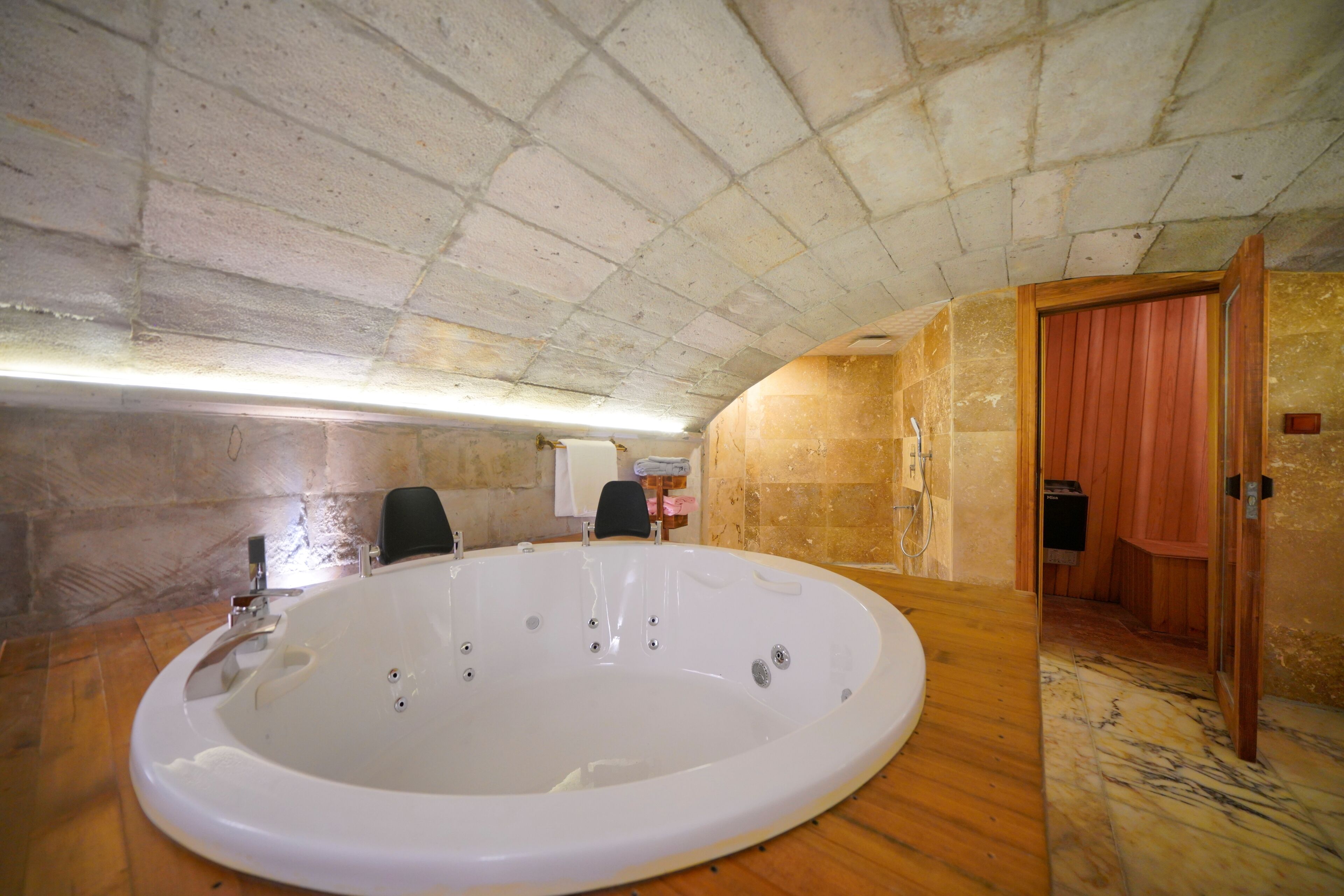 A large, oval-shaped hot tub in a room with a high, arched ceiling and stone walls.