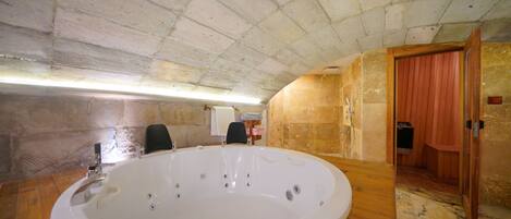 A large, oval-shaped hot tub in a room with a high, arched ceiling and stone walls.
