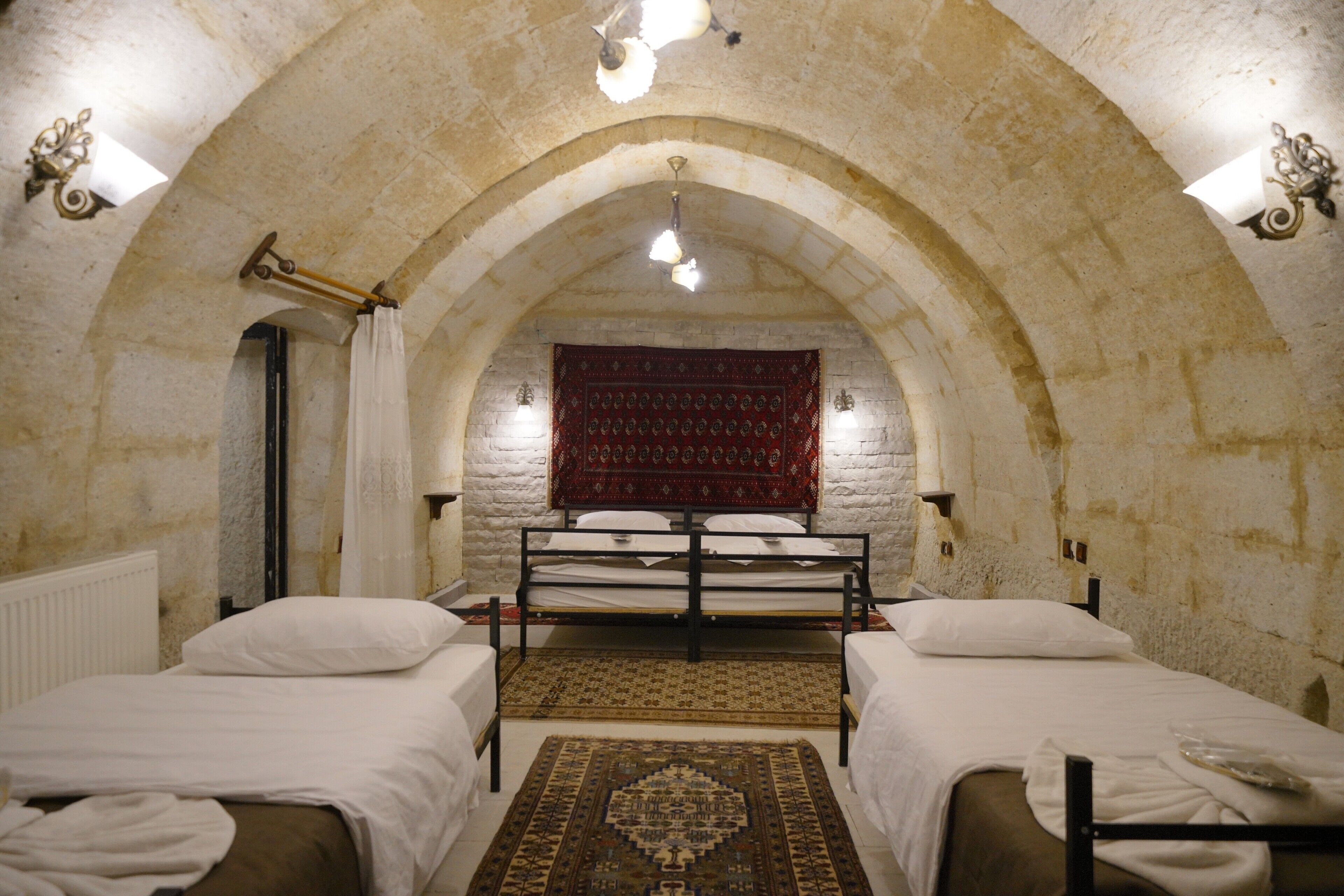 A room with two beds, a red patterned tapestry, and stone walls.
