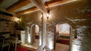 A rustic interior with stone walls, wooden beams, and a cozy seating area with a chair and a small table.