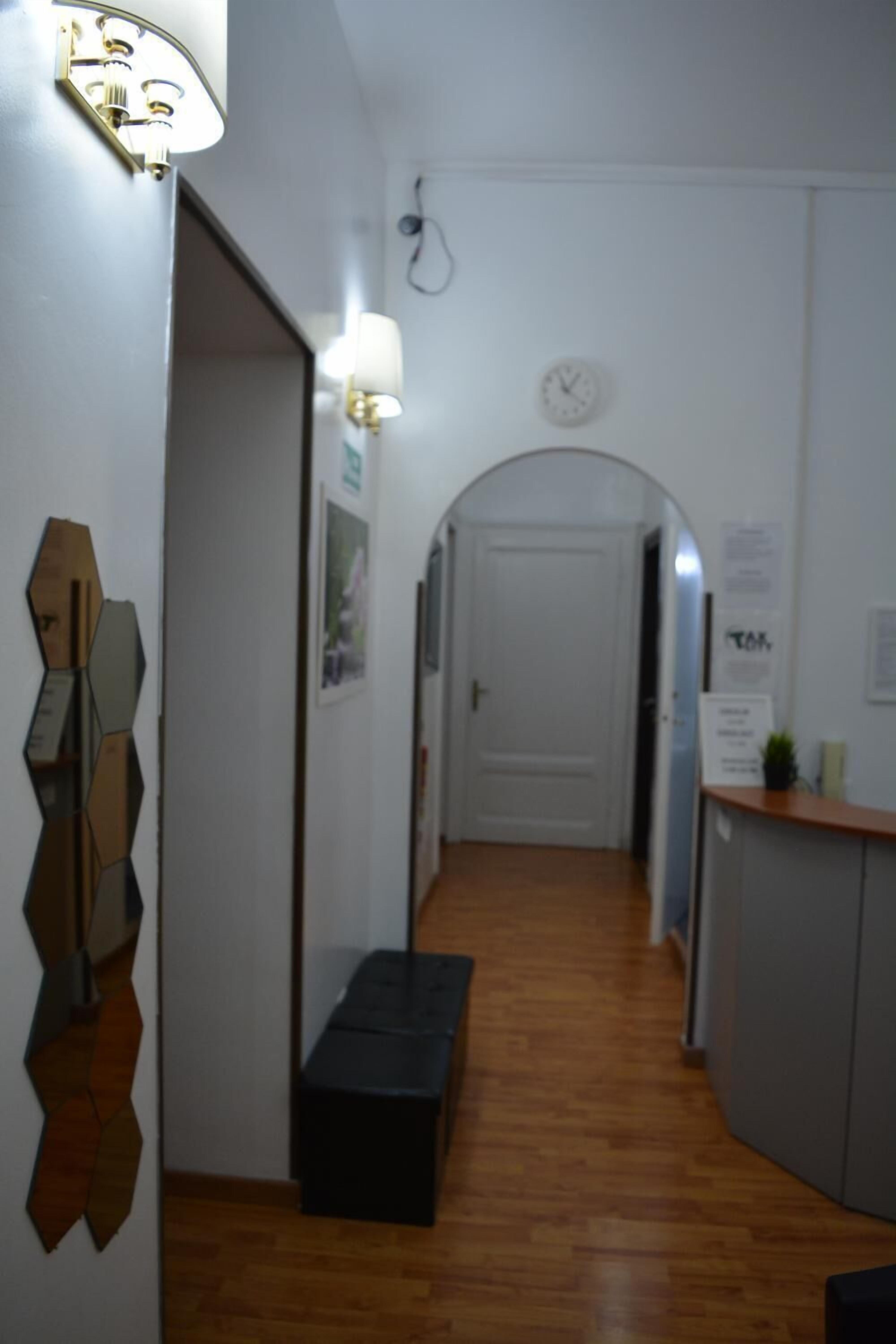 A hallway with a wooden floor, a bench, a reception desk, and a door at the end.