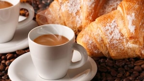 A cup of coffee on a saucer with a croissant in the background. - Locanda Otello (Rome)