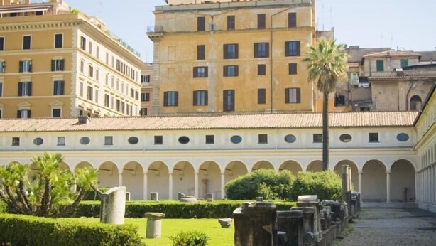 A courtyard with a row of arches, a palm tree, and a building with multiple windows. - Locanda Otello (Rome)