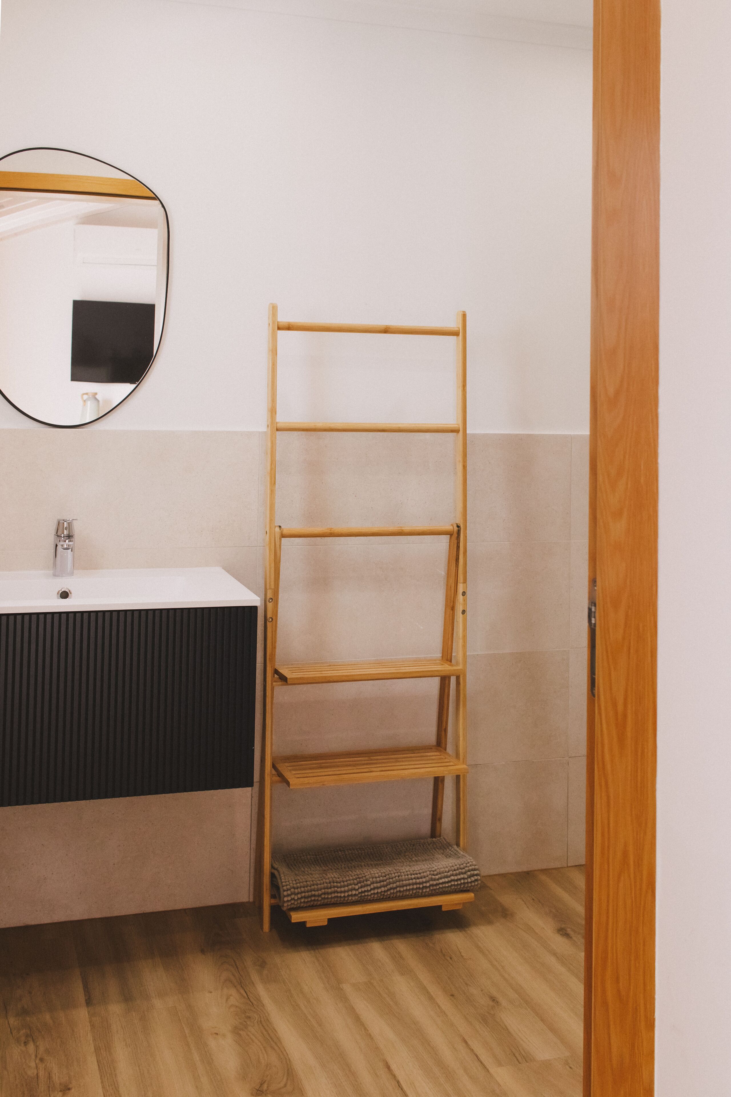 A bathroom with a wooden shelf unit, a sink, and a mirror.
