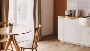 A kitchen with white cabinets, a wooden dining table, and a hanging wicker light fixture. - Pure Flor de Esteva (Vila do Bispo)