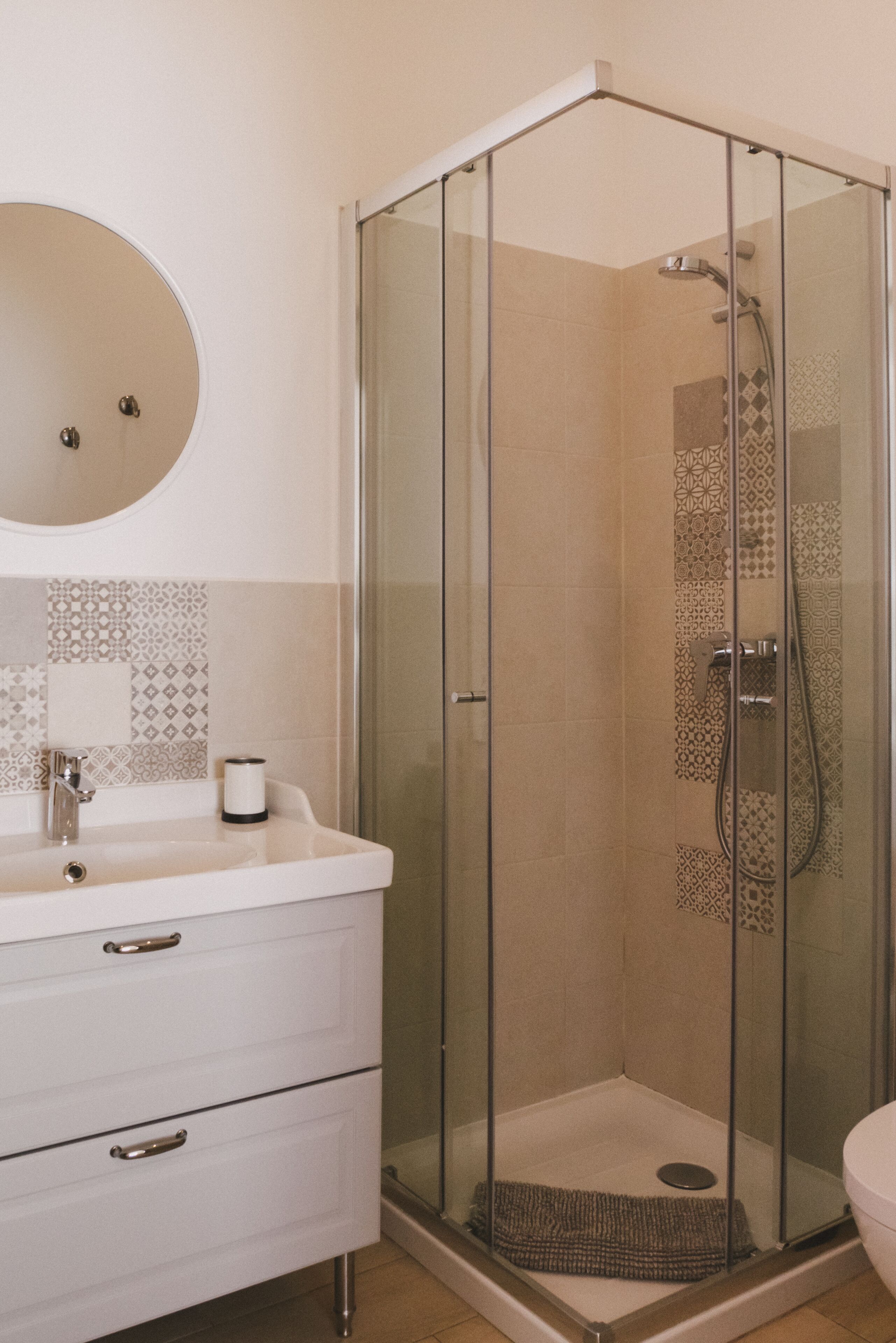A modern bathroom with a glass-enclosed shower, a white sink with a mirror, and patterned tiles.