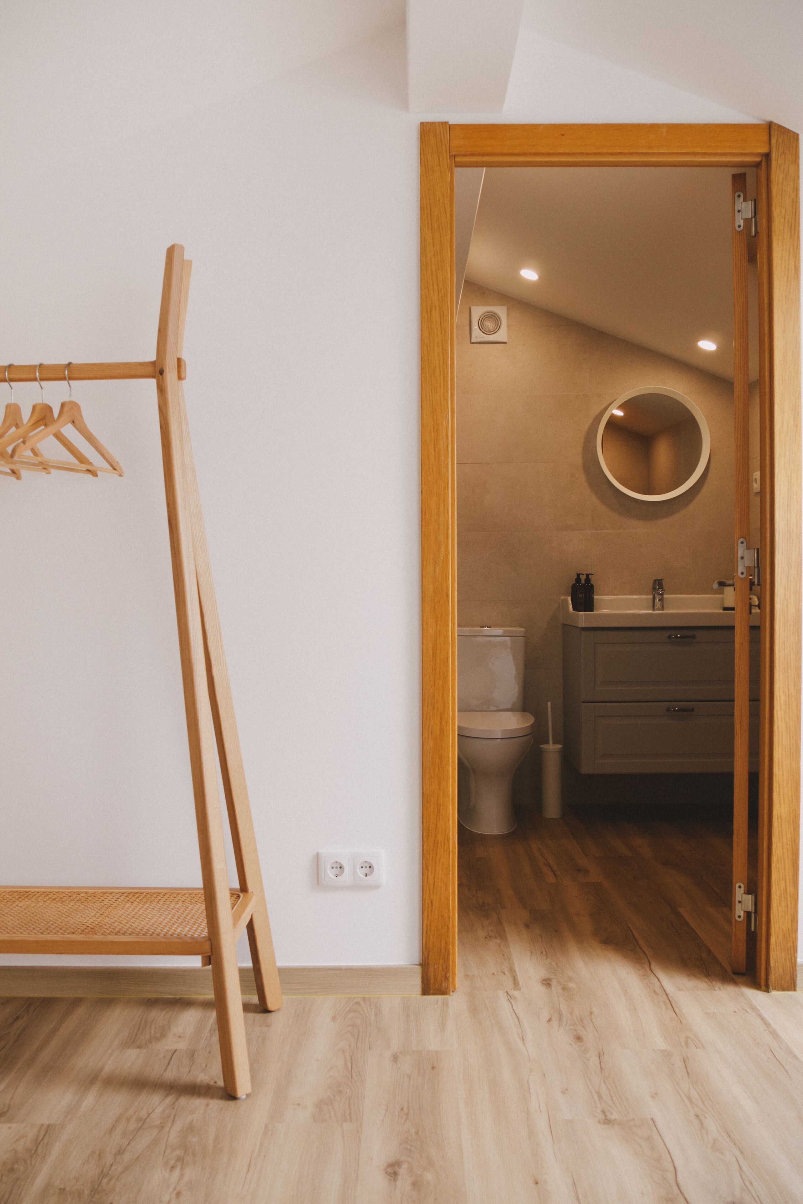 Un perchero de madera, un inodoro, un lavabo y un espejo en un baño.