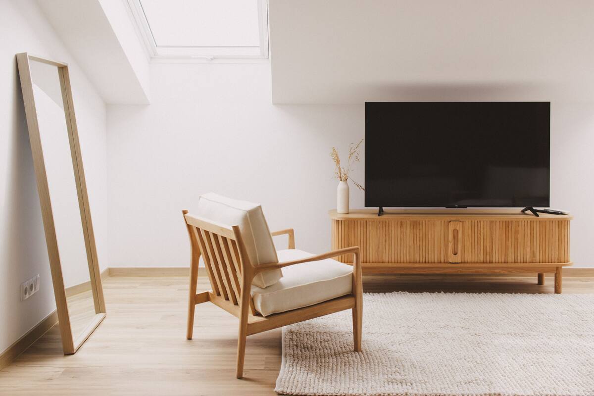 A modern living room with a wooden chair, a large flat-screen TV, and a white cabinet.
