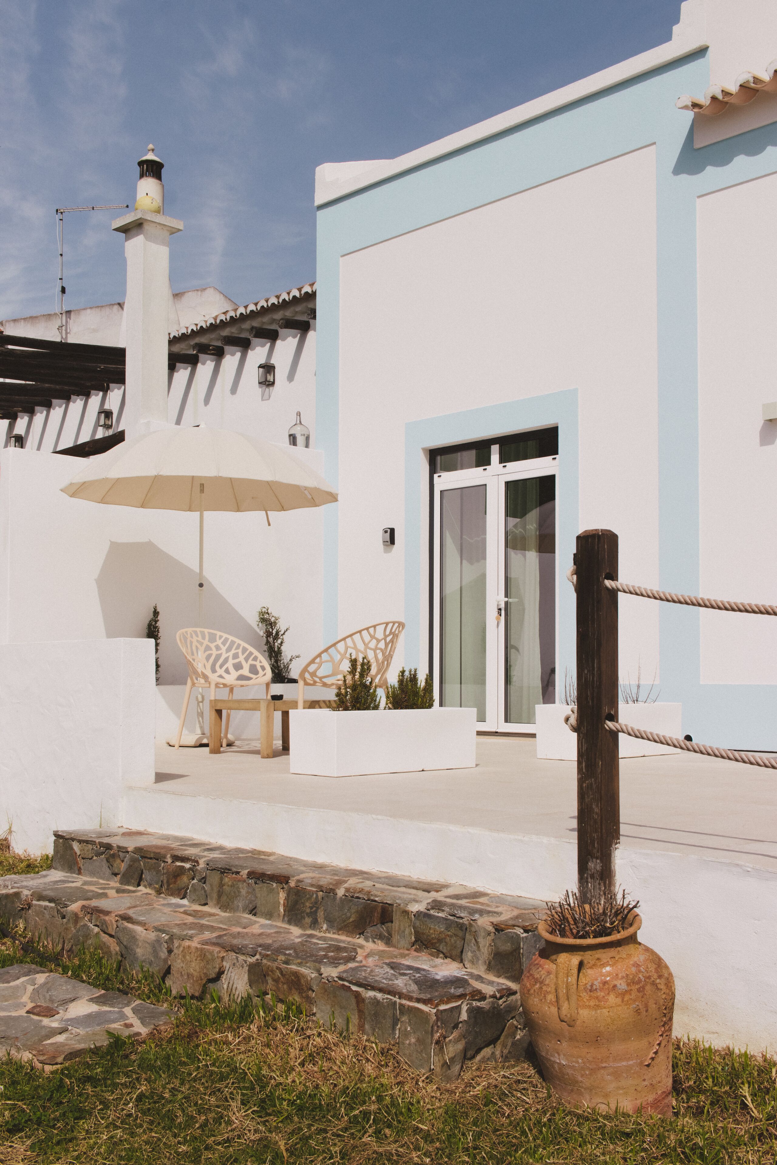 A white building with a blue trim, a large umbrella, and two chairs outside.