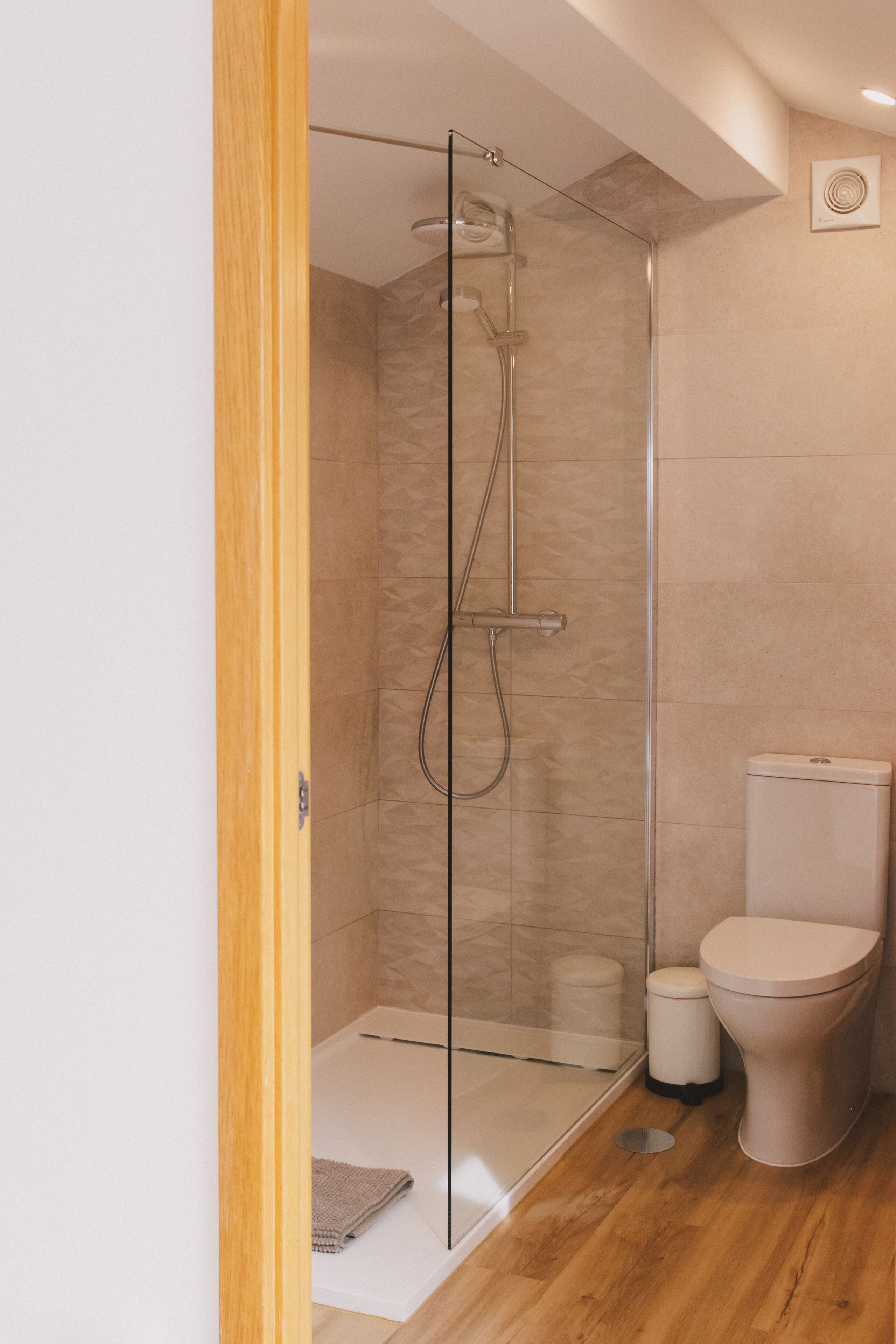 A modern bathroom with a glass-enclosed shower, a toilet, and a wooden floor.