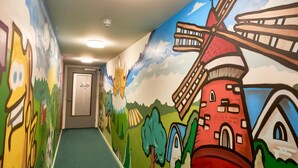 A colorful mural on a hallway wall depicting a windmill, a church, and a farm scene. - Hotel Villa GROET uit Avenhorn (Avenhorn)