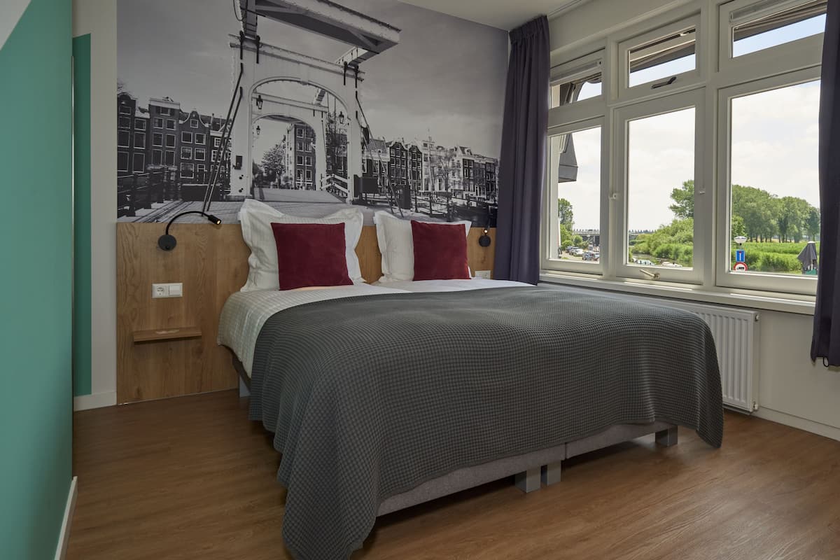 A bedroom with a large bed, a mural of a cityscape, and a window with a view of greenery.