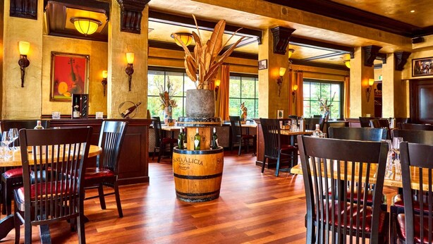 A restaurant with wooden tables and chairs, a large wooden barrel centerpiece, and warm lighting. - Hotel Villa GROET uit Avenhorn (Avenhorn)