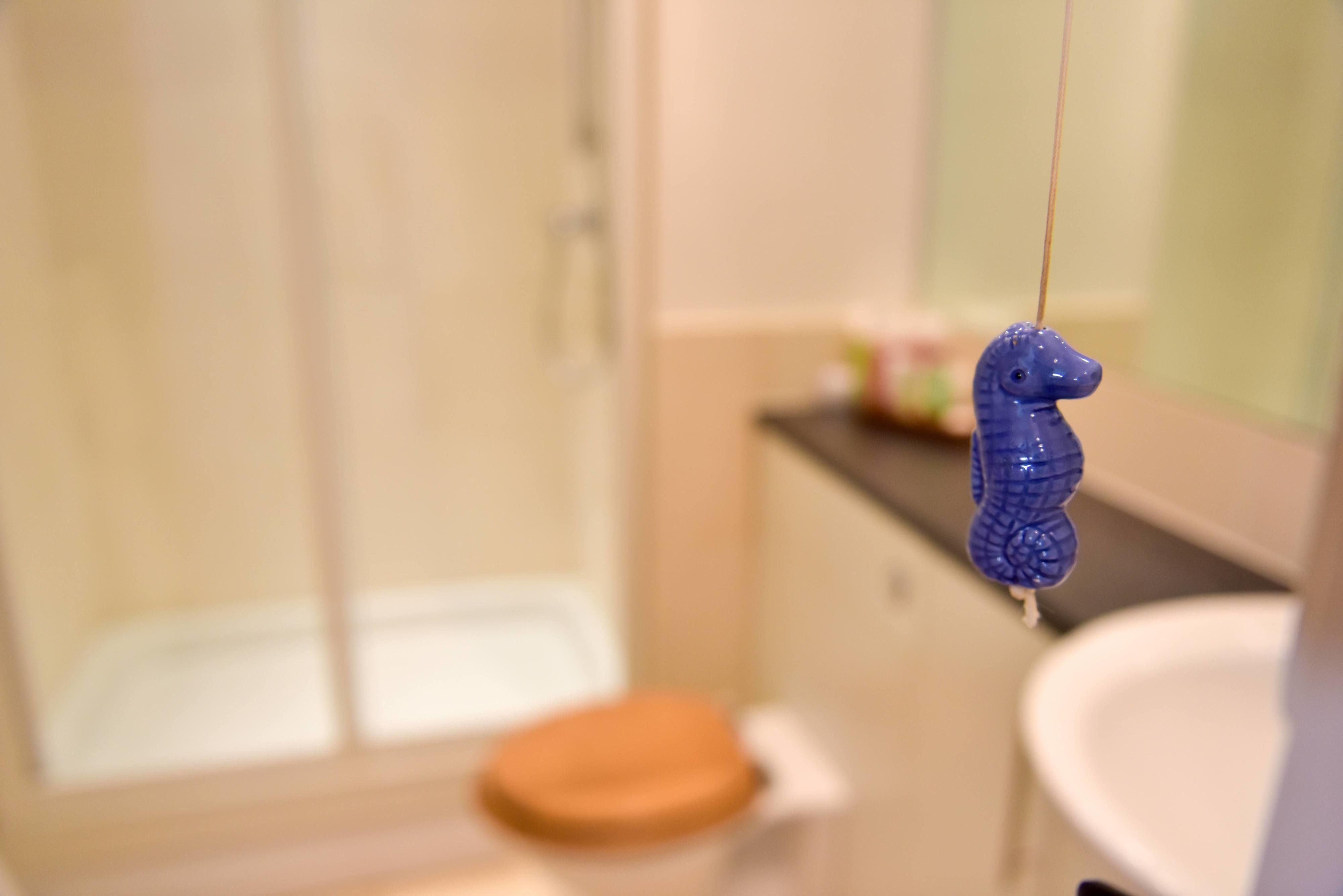 A bathroom with a glass shower enclosure, a white sink, and a blue seahorse hanging ornament.