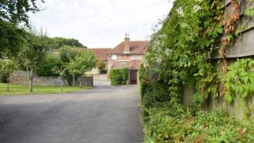 A narrow driveway leading to a brick house with a chimney, surrounded by lush greenery and a stone wall.