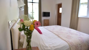 Une chambre à coucher avec un lit, une table de chevet, une lampe, un téléviseur fixé au mur et une fenêtre avec des rideaux.
