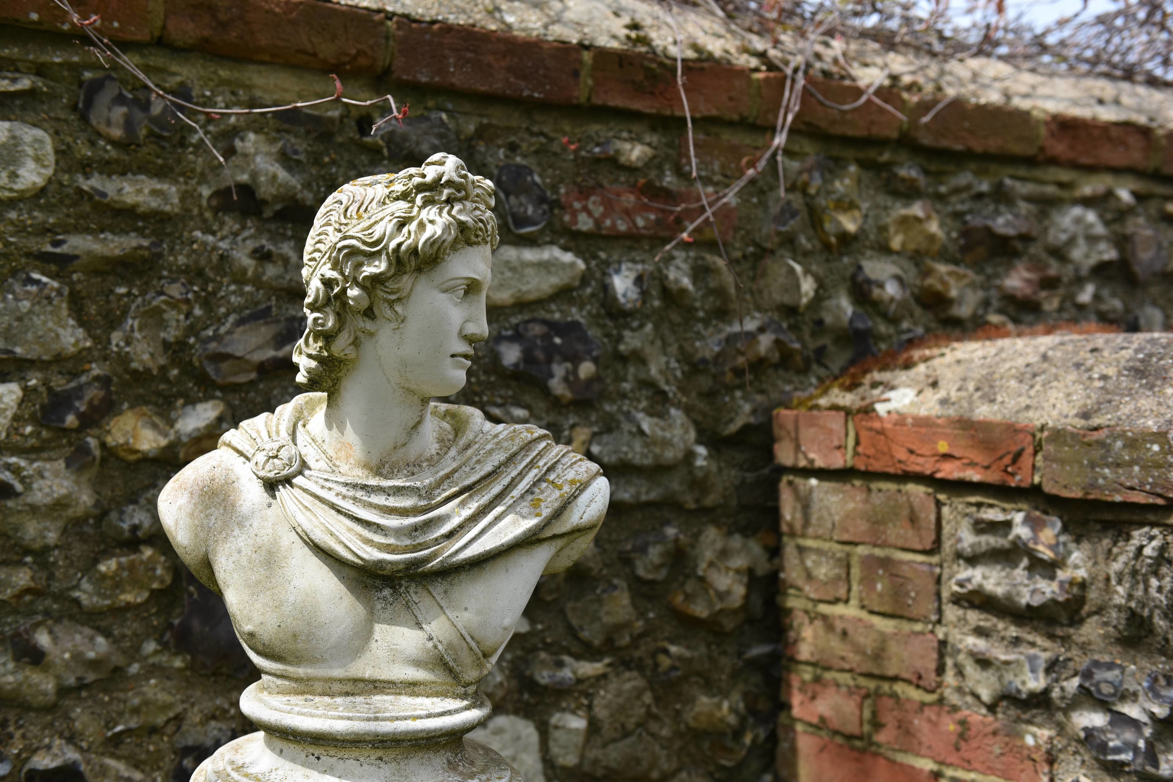 Une sculpture en buste adossée à un mur de pierre.