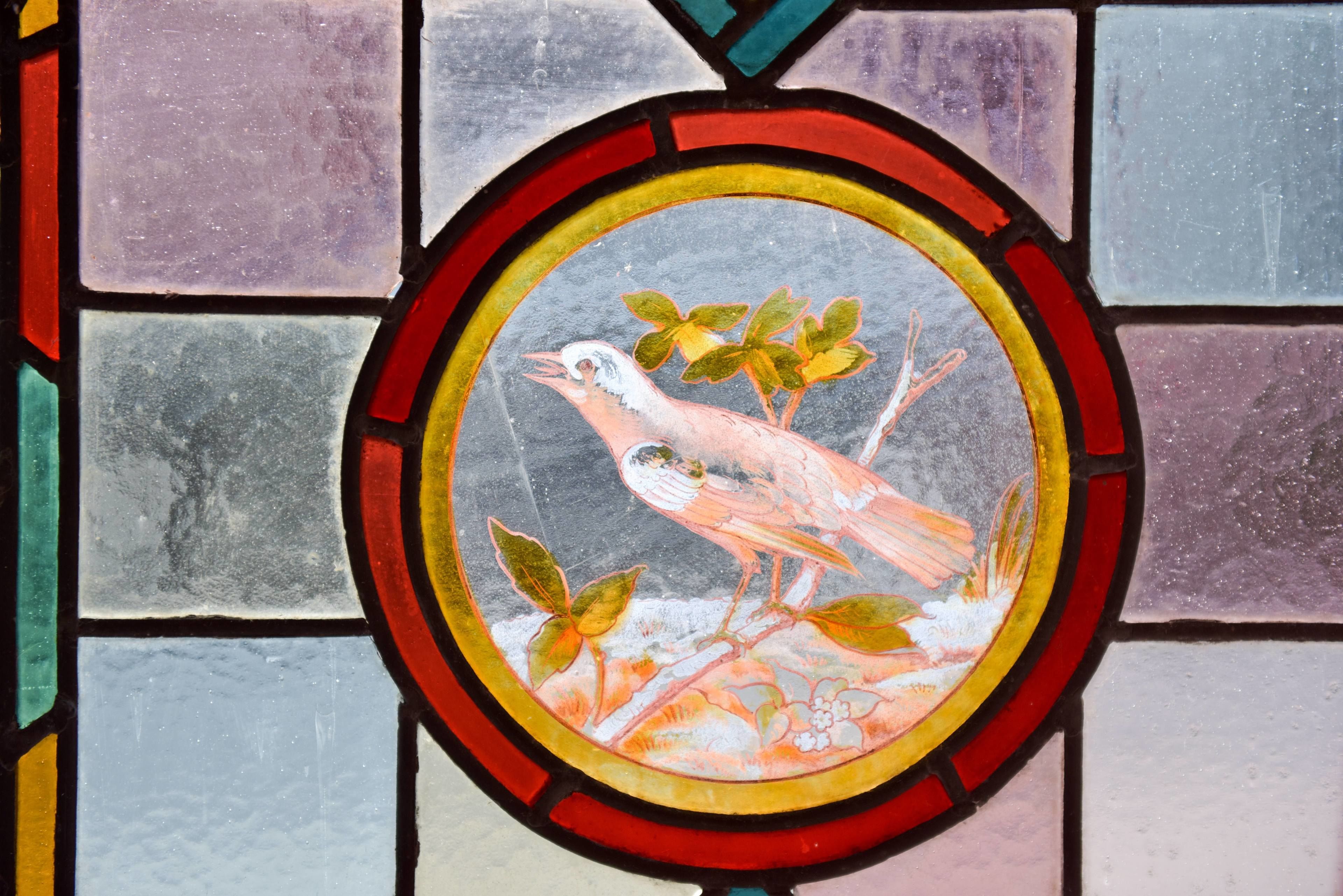 A stained glass window with a bird and foliage design.