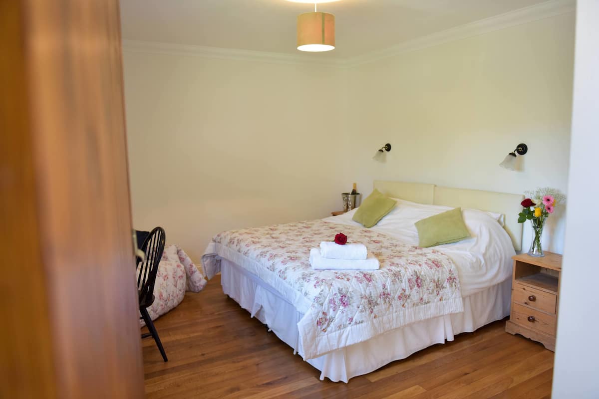 A neatly arranged bedroom with a bed, a nightstand, a chair, and a bedside table.