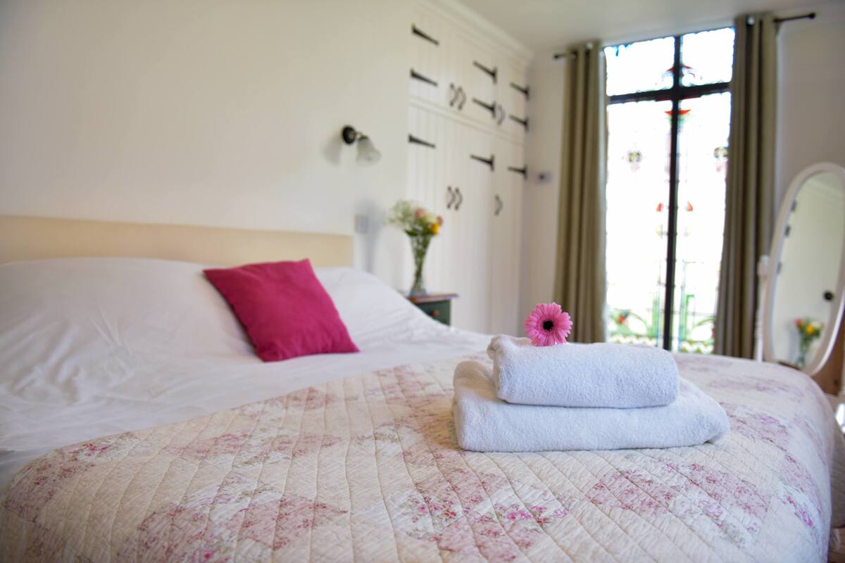 A neatly made bed with a floral quilt, a pink pillow, and two folded towels.