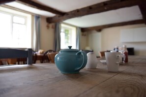 Una mesa de madera con una tetera azul verdosa, una taza blanca y una jarra blanca en una cocina.