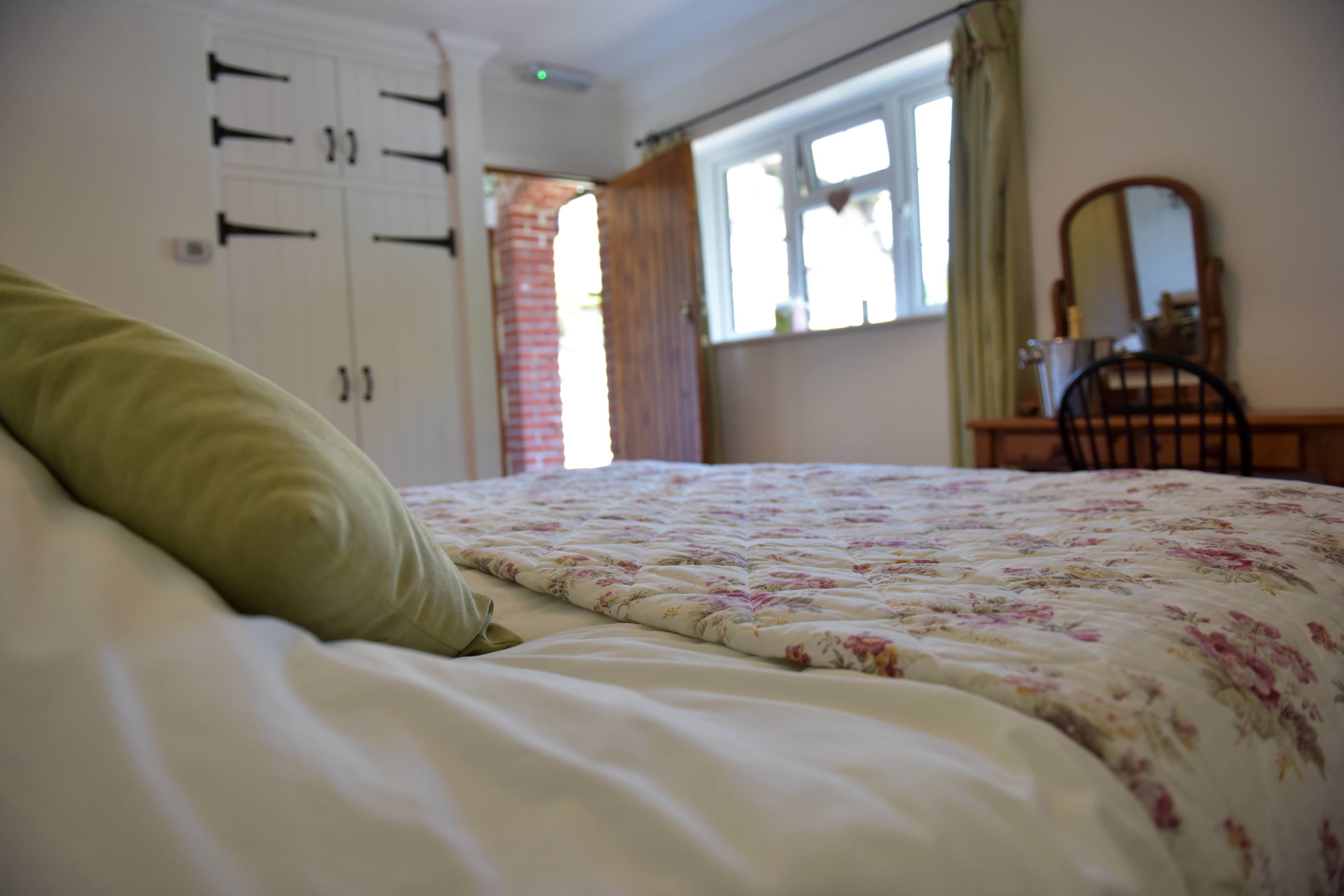 Una camera da letto con un letto, un armadio, una finestra con tende e uno specchio su una cassettiera.