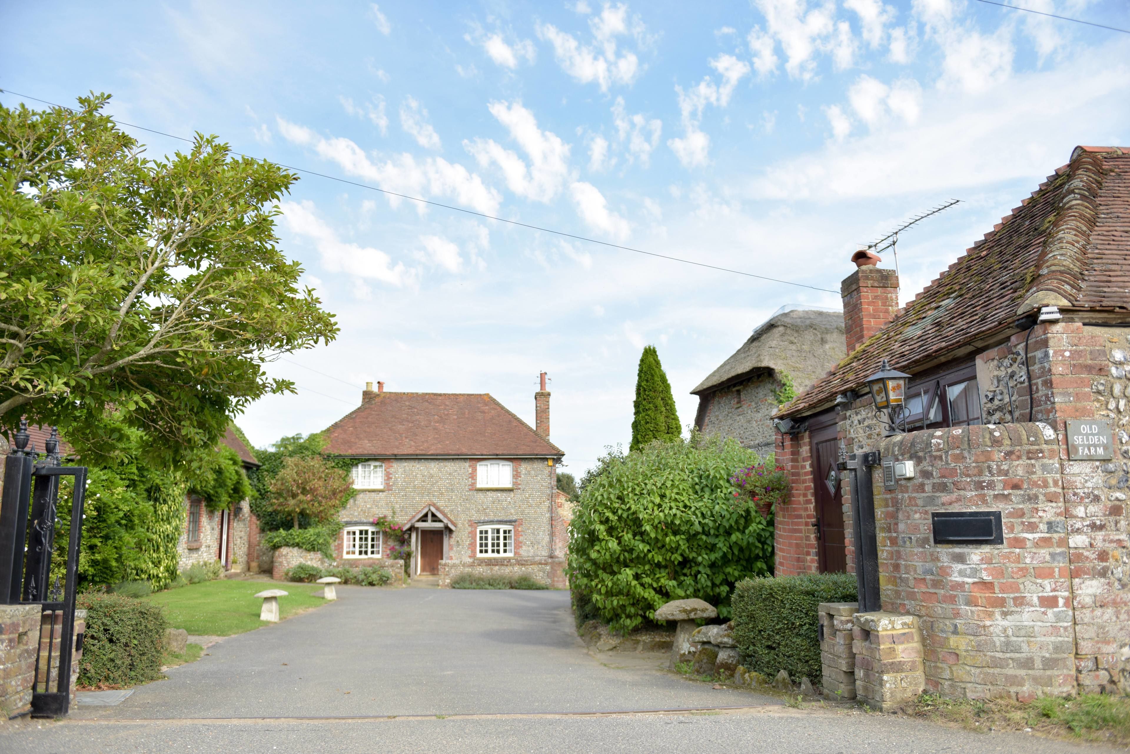 A rural street with a traditional brick house, a stone wall, and a gate.