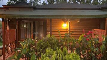 Una cabaña de madera con porche, un espacio de estar cubierto y un jardín con diversas plantas y flores.