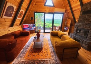A cozy living room with a wooden ceiling, a stone fireplace, and a large window offering a view of the outdoors. - Agva Green River Otel - Adults Only (Sile)