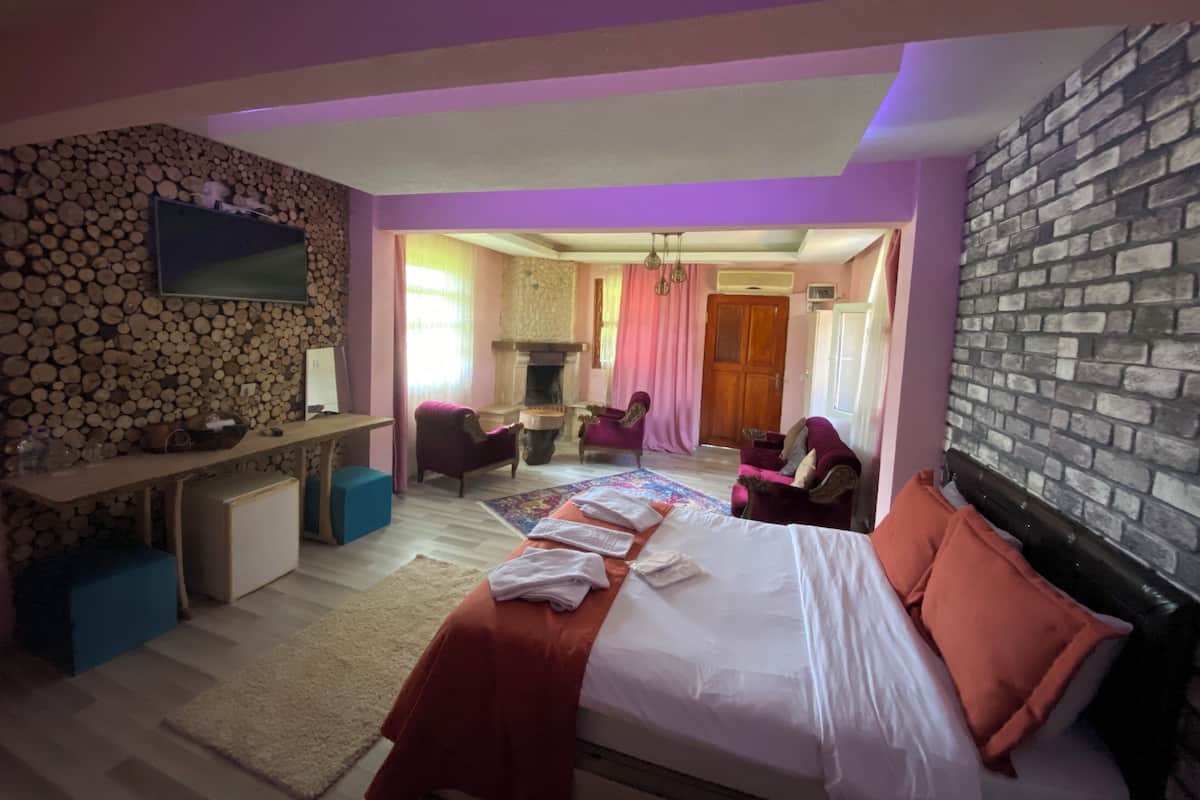 A bedroom with a bed, a desk, chairs, a fireplace, and a stone wall.
