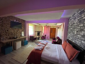 Un dormitorio con cama, escritorio, sillas, chimenea y pared de piedra.